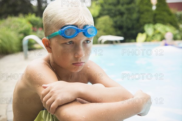 Upset Caucasian boy sitting near swimming pool