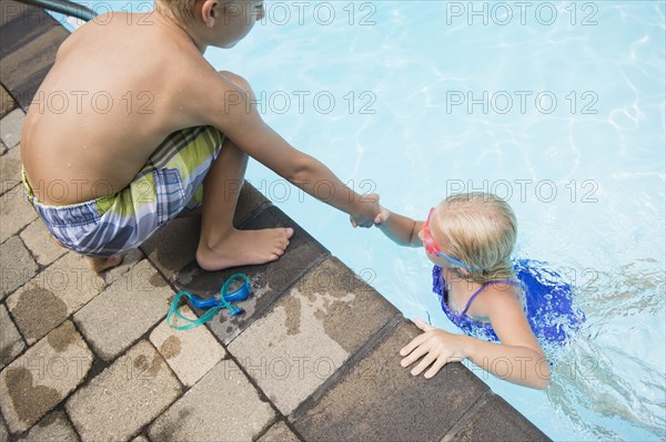 Caucasian boy helping sister out of swimming pool