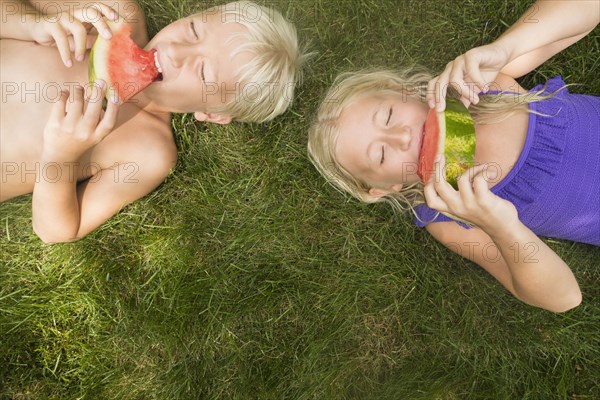 Caucasian children eating watermelon on lawn