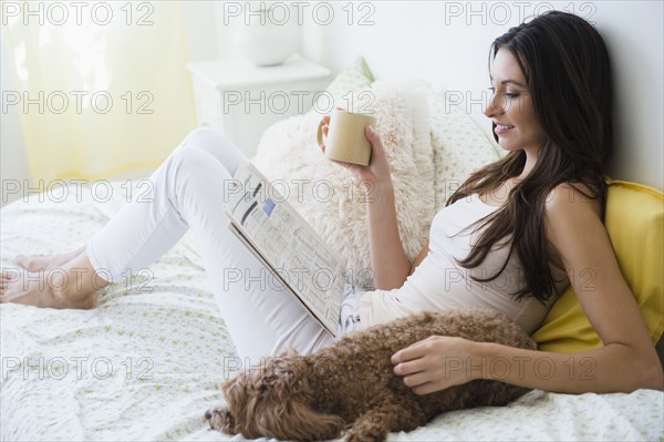 Caucasian woman reading magazine with pet dog in bed