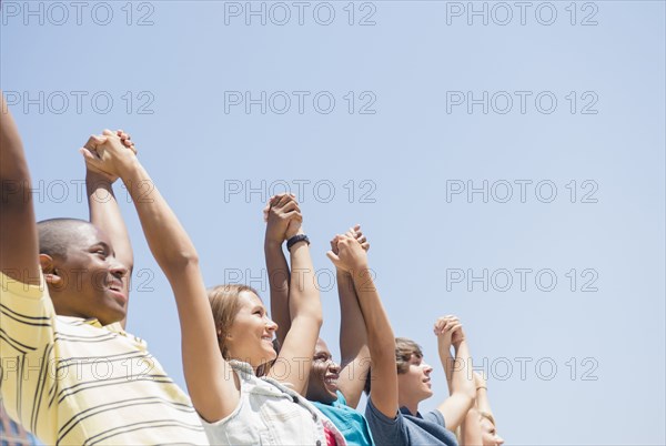 Low angle view of teenagers holding hands under blue sky