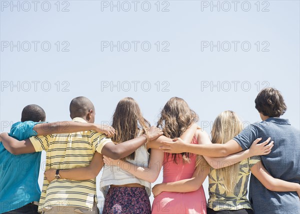 Rear view of teenagers hugging under blue sky