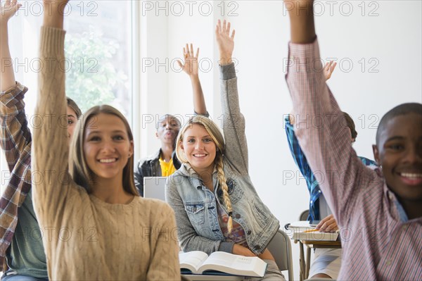 Teenage students raising hands in classroom