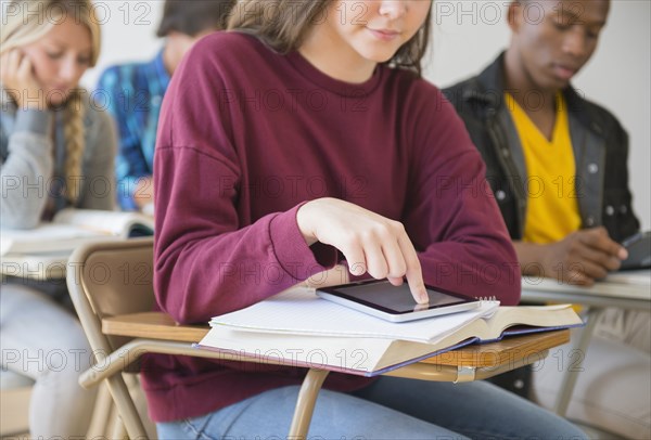 Teenage student using digital tablet on desk in classroom