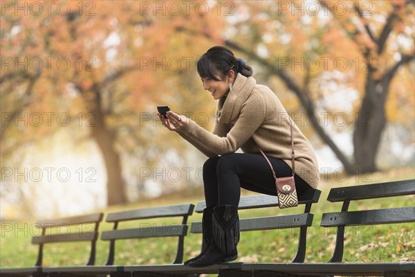 Asian woman using cell phone on park bench