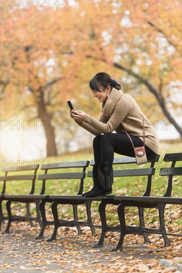 Asian woman using cell phone on park bench