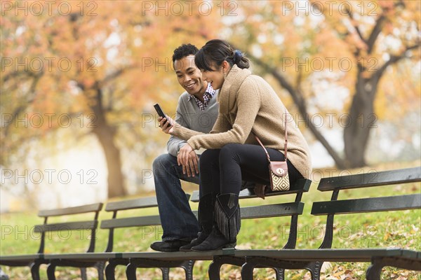 Couple using cell phone on park bench