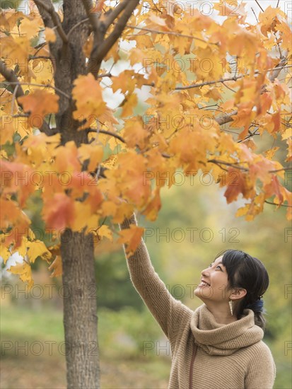 Asian woman reaching for autumn leaves in park