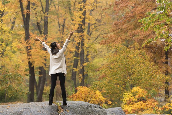 Asian woman cheering with arms outstretched on rock in park