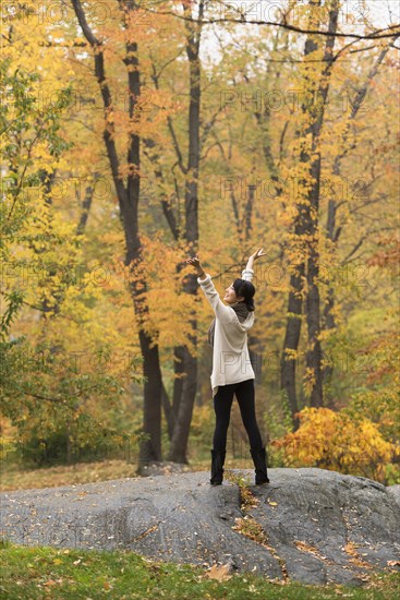 Asian woman cheering with arms outstretched on rock in park