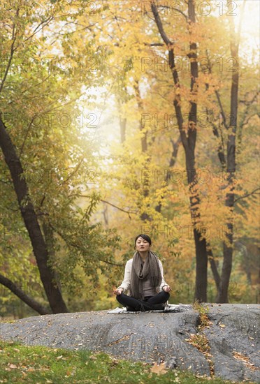 Asian woman meditating on rock in park