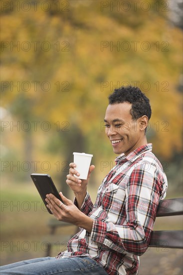 Mixed race man using digital tablet on park bench