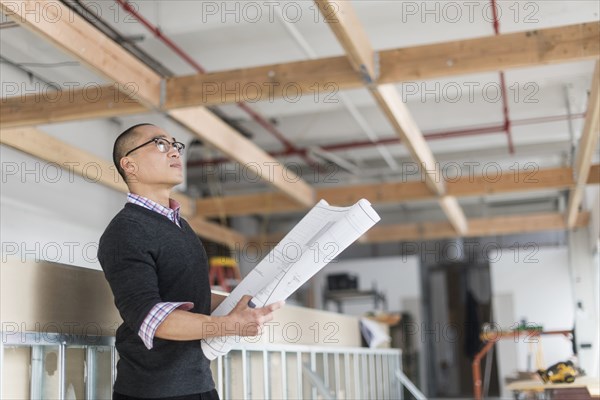 Korean architect holding blueprints and examining ceiling