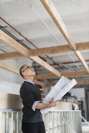 Korean architect holding blueprints and examining ceiling