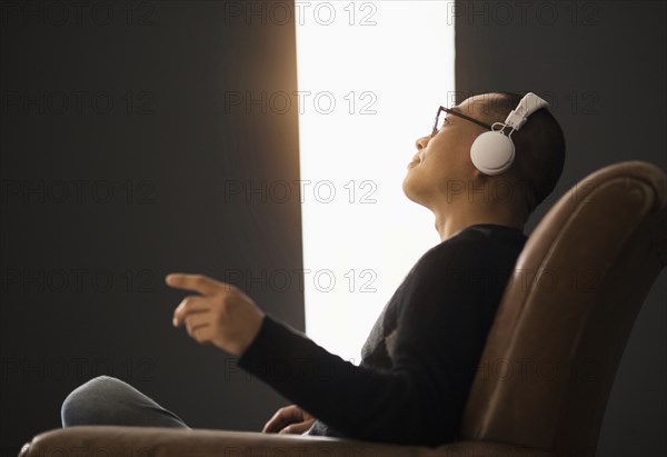 Korean man listening to headphones in armchair