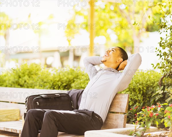 Black businessman relaxing on bench outdoors