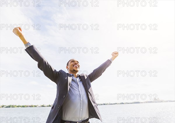 Black businessman cheering with arms outstretched outdoors