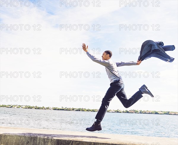 Black businessman running on waterfront wall outdoors