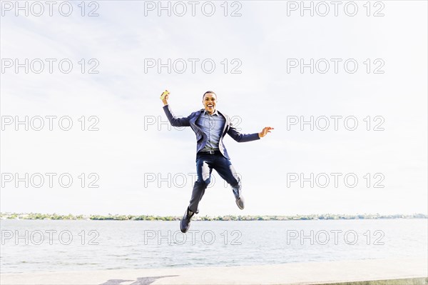 Black businessman jumping for joy at waterfront