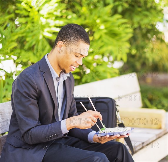 Black businessman eating sushi on park bench