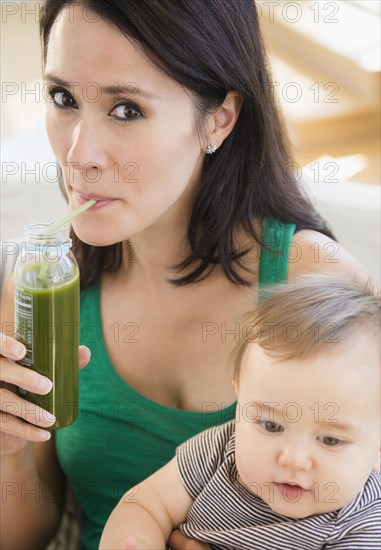 Close up of mixed race mother holding baby and drinking green juice