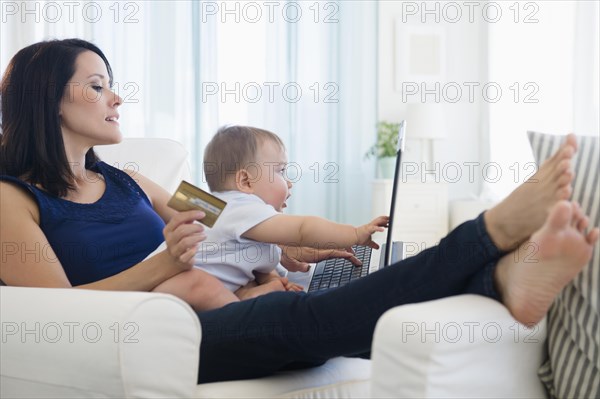 Mixed race mother holding baby and shopping on laptop