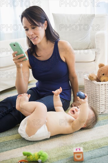 Mixed race mother using cell phone with baby on floor