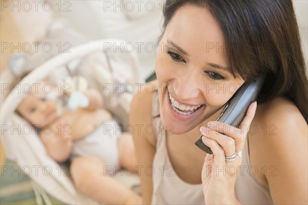 Close up of mixed race mother talking on telephone near baby