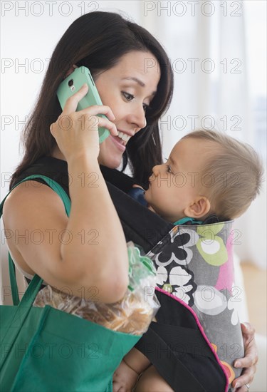 Mixed race mother carrying baby and talking on cell phone