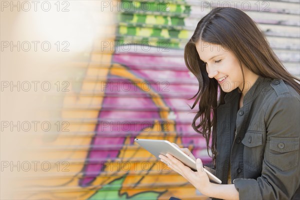 Caucasian woman using digital tablet near graffiti wall