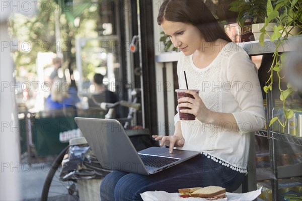 Caucasian woman using laptop and drinking coffee outside cafe