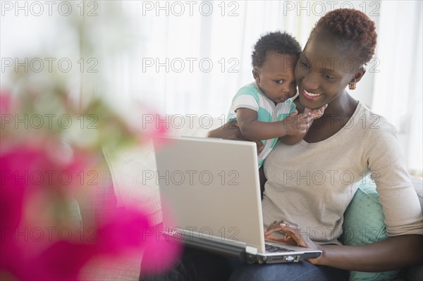 Black mother and son using laptop on sofa