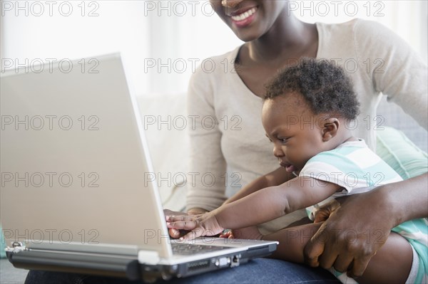 Black mother and son using laptop on sofa