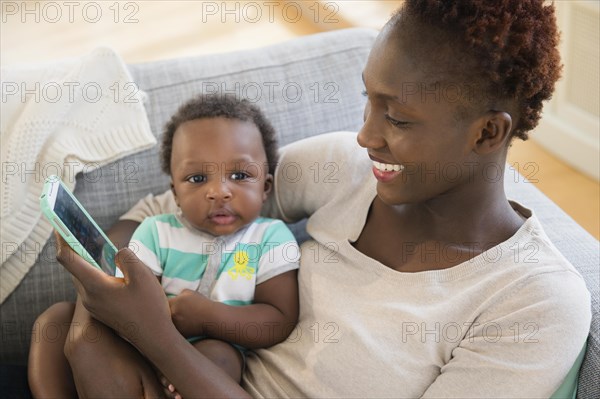 Black mother and son using cell phone on sofa