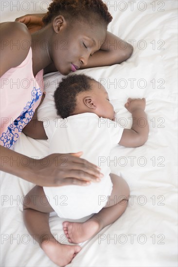 Black mother and son sleeping on bed