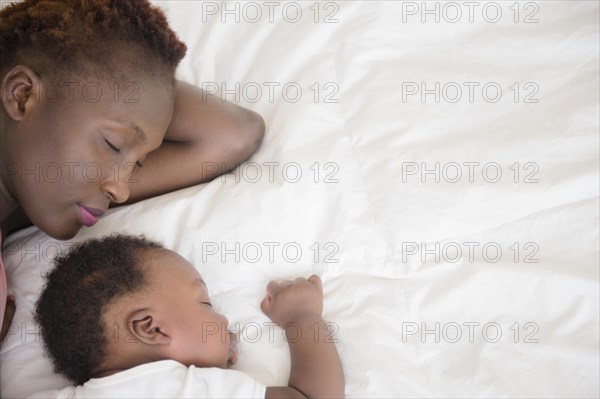 Black mother and son sleeping on bed