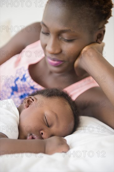 Black mother admiring sleeping son on bed