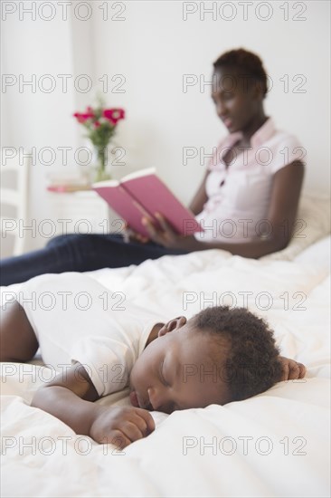 Black mother reading near sleeping baby boy