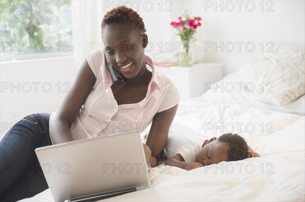 Black mother using laptop near sleeping baby boy