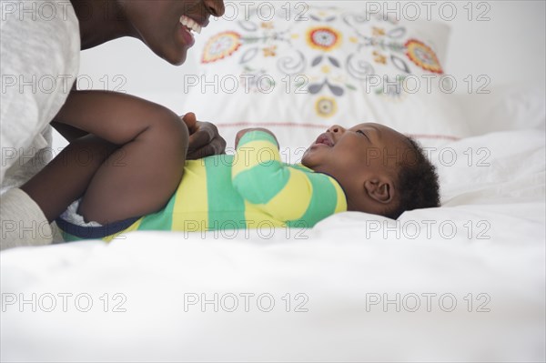 Black mother playing with baby boy on bed