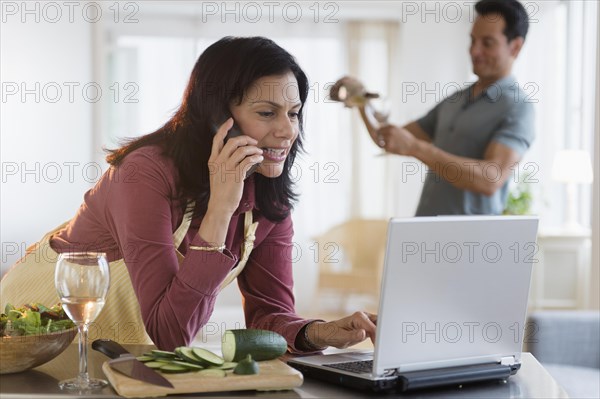 Woman working and cooking dinner with husband pouring wine