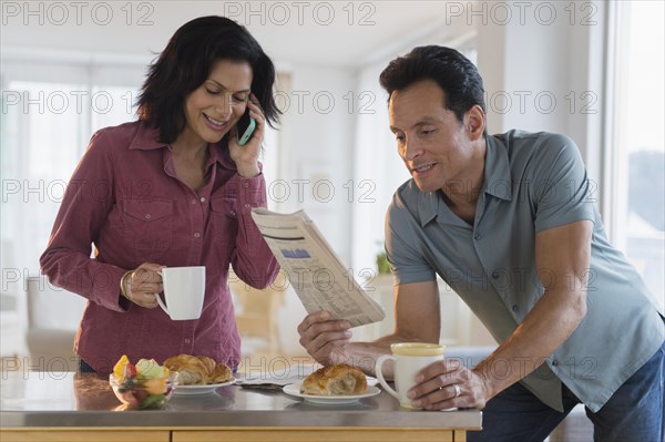 Couple reading newspaper and talking on cell phone at breakfast