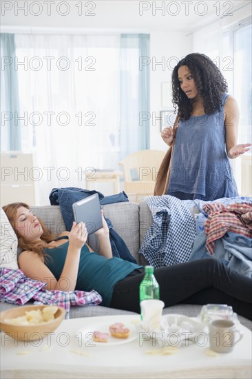 Woman frustrated at lazy roommate using digital tablet on sofa