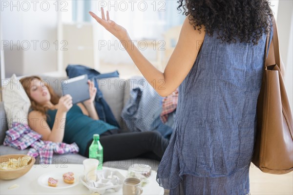 Woman frustrated at lazy roommate using digital tablet on sofa