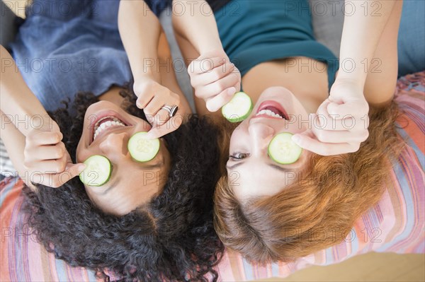 Women holding cucumber slices over eyes