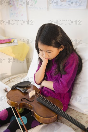 Pouting Vietnamese girl holding violin in bedroom