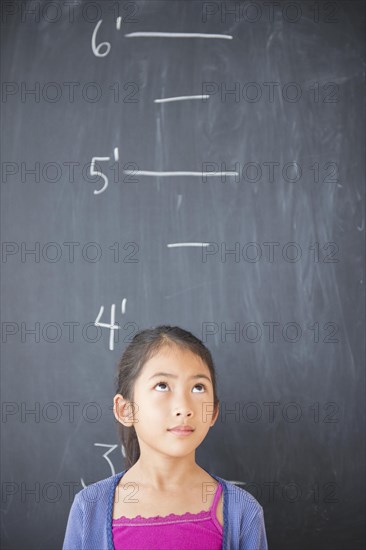 Vietnamese student standing under height markers on chalkboard