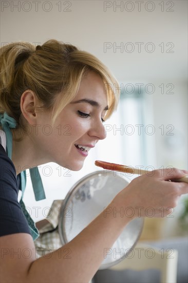 Caucasian woman tasting sauce while cooking in kitchen
