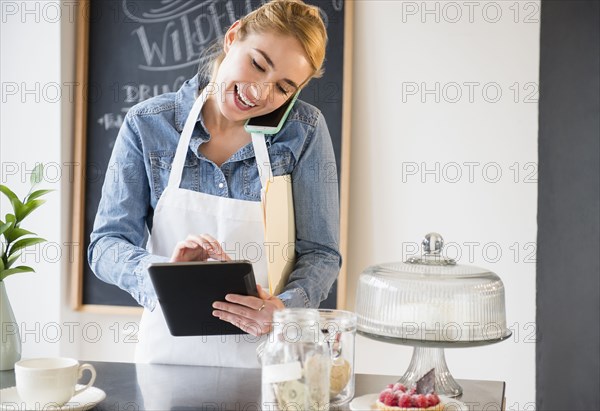 Caucasian barista using cell phone and digital tablet in cafe