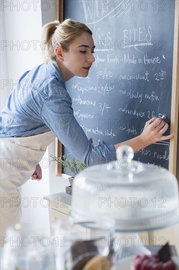 Caucasian barista writing menu on cafe chalkboard